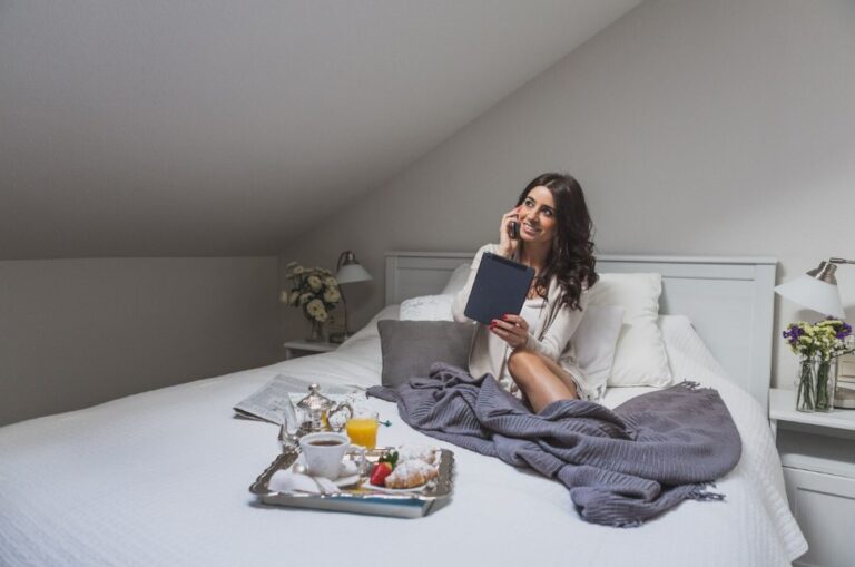 a young woman talking on the phone and holding a tablet while sitting on a bed